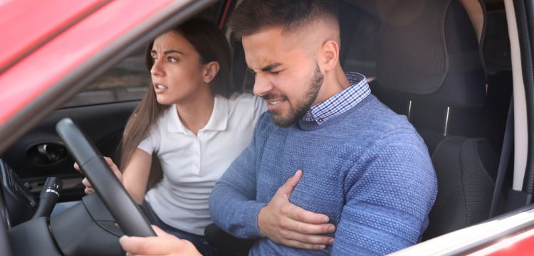 In the driver's seat, a man grabs his chest after an accident while sitting in his red car