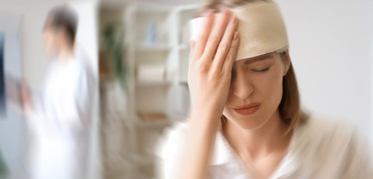 Woman at the doctor's office with head wrapped in gauze and holding her hand pressed against her head.